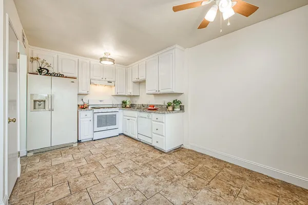 a kitchen with granite countertop a refrigerator a sink dishwasher and white cabinets with wooden floor