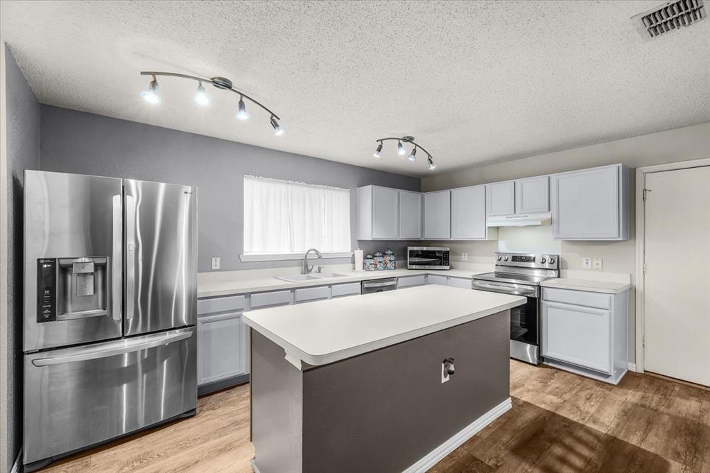 Kitchen with appliances with stainless steel finishes, light countertops, a kitchen island, light wood-style floors, and a textured ceiling