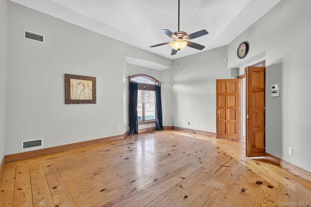 a view of an empty room with wooden floor and a ceiling fan