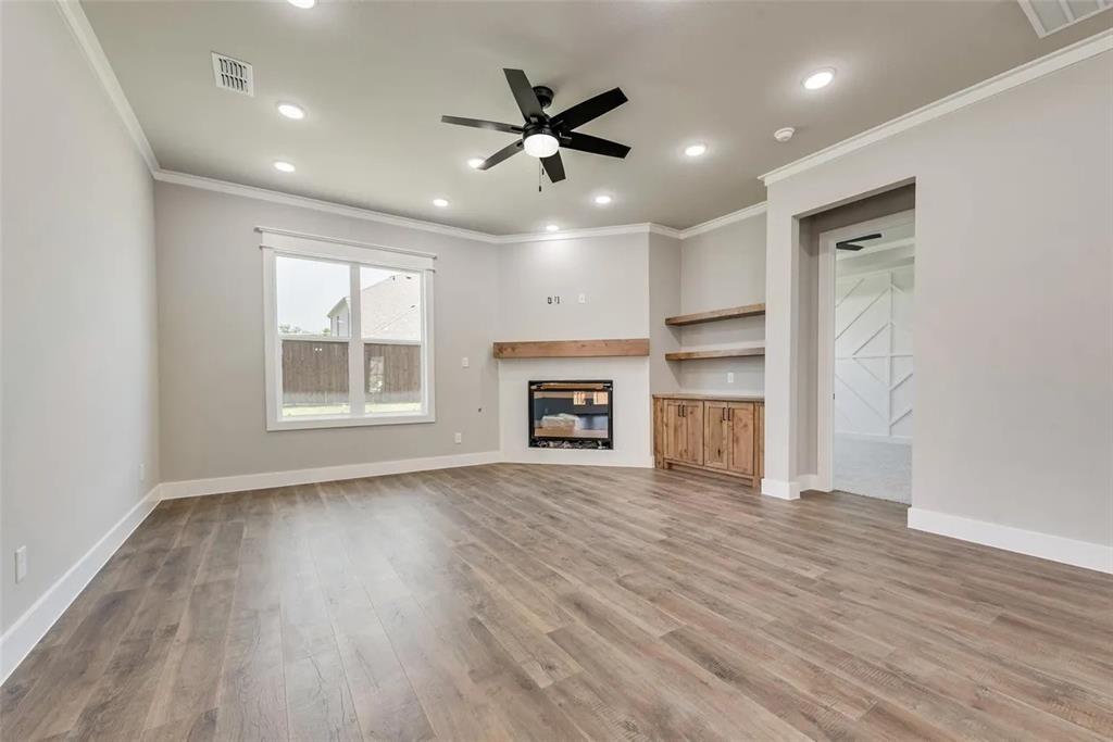 1327 Selby Road Van Alstyne, TX 75495 - Photo 9 of 32 Unfurnished living room with a ceiling fan, a glass covered fireplace, crown molding, light wood-style floors, and recessed lighting