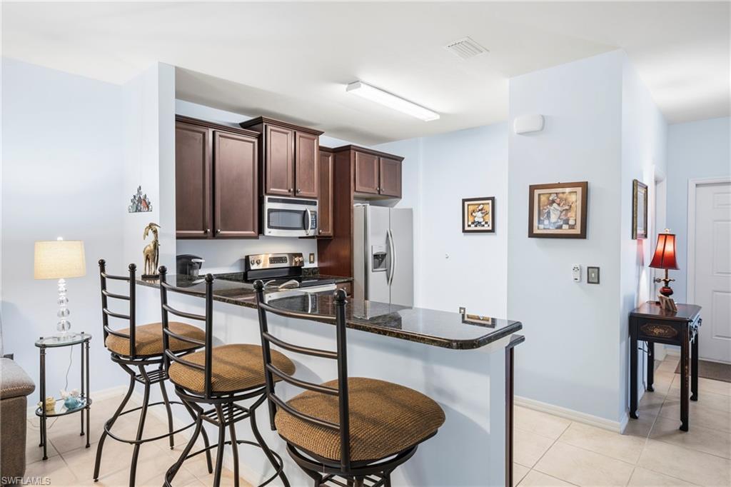 3916 Cherrybrook Loop Fort Myers, FL 33966 - Photo 5 of 31 Kitchen area featuring a granite-style countertop breakfast bar, dark wood-finish cabinetry, a stainless steel microwave, and a stainless steel refrigerator
