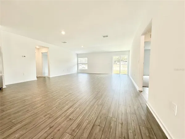 a view of an empty room with wooden floor and a kitchen