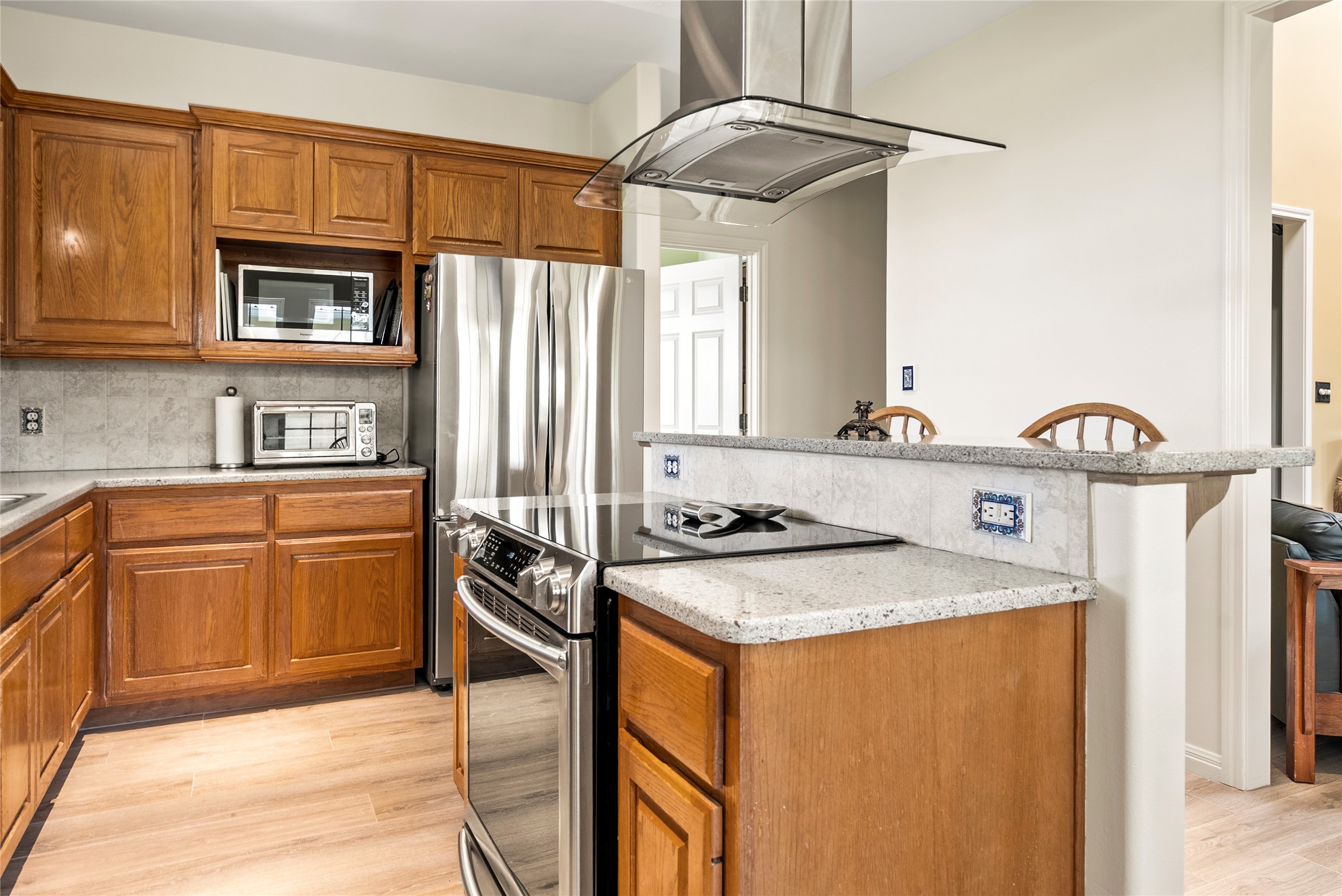 928 Upper Elgin River Road Elgin, TX 78621 - Photo 16 of 40 Kitchen featuring wood-finish cabinetry, stainless steel appliances, light granite countertops, and a stone-finish tile backsplash.