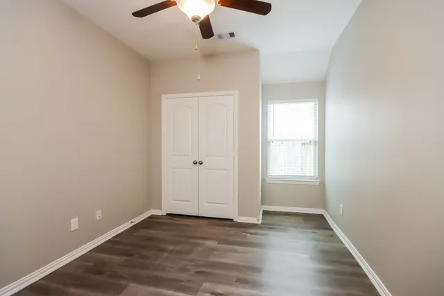an empty room with wooden floor chandelier fan and windows