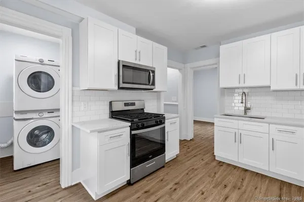 a kitchen with stainless steel appliances granite countertop a stove a white cabinets a sink and dishwasher with wooden floor