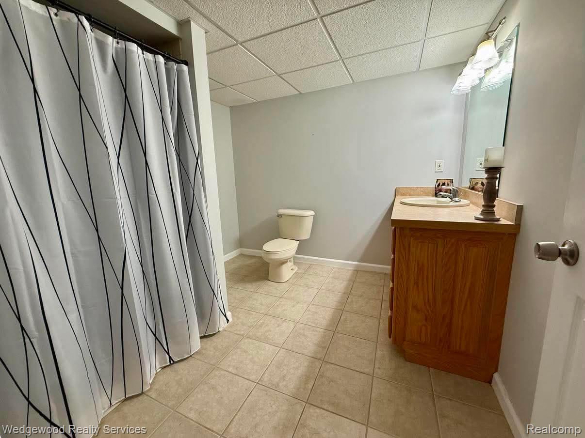 492 Harvard Drive, Unit 84 Romeo, MI 48065 - Photo 28 of 30 Tile flooring, light wood-finish vanity with integrated sink, wall-mounted vanity lighting, and drop ceiling
