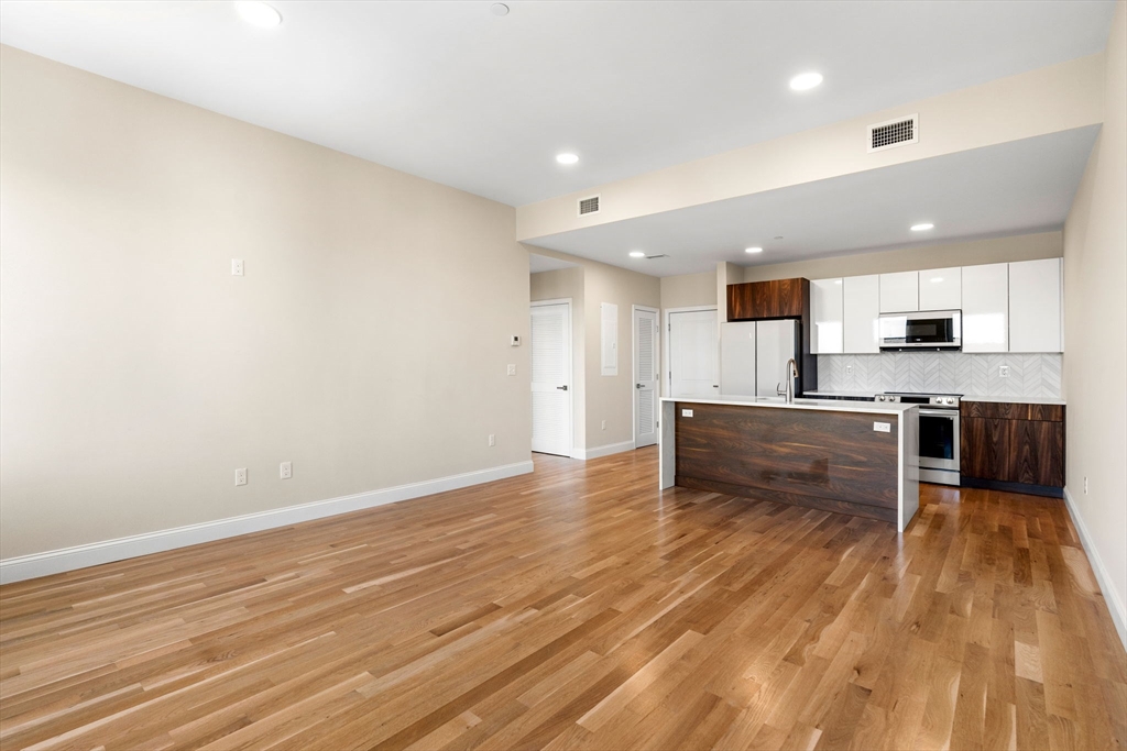 16 Taber Street, Unit 304 Boston, MA 02119 - Photo 8 of 11 an empty room with wooden floor and kitchen view