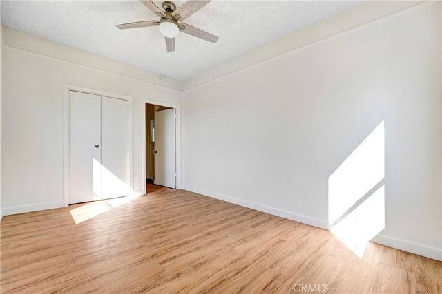 a view of an empty room with wooden floor and a ceiling fan