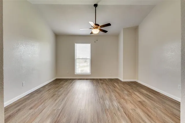 an empty room with wooden floor chandelier fan and windows