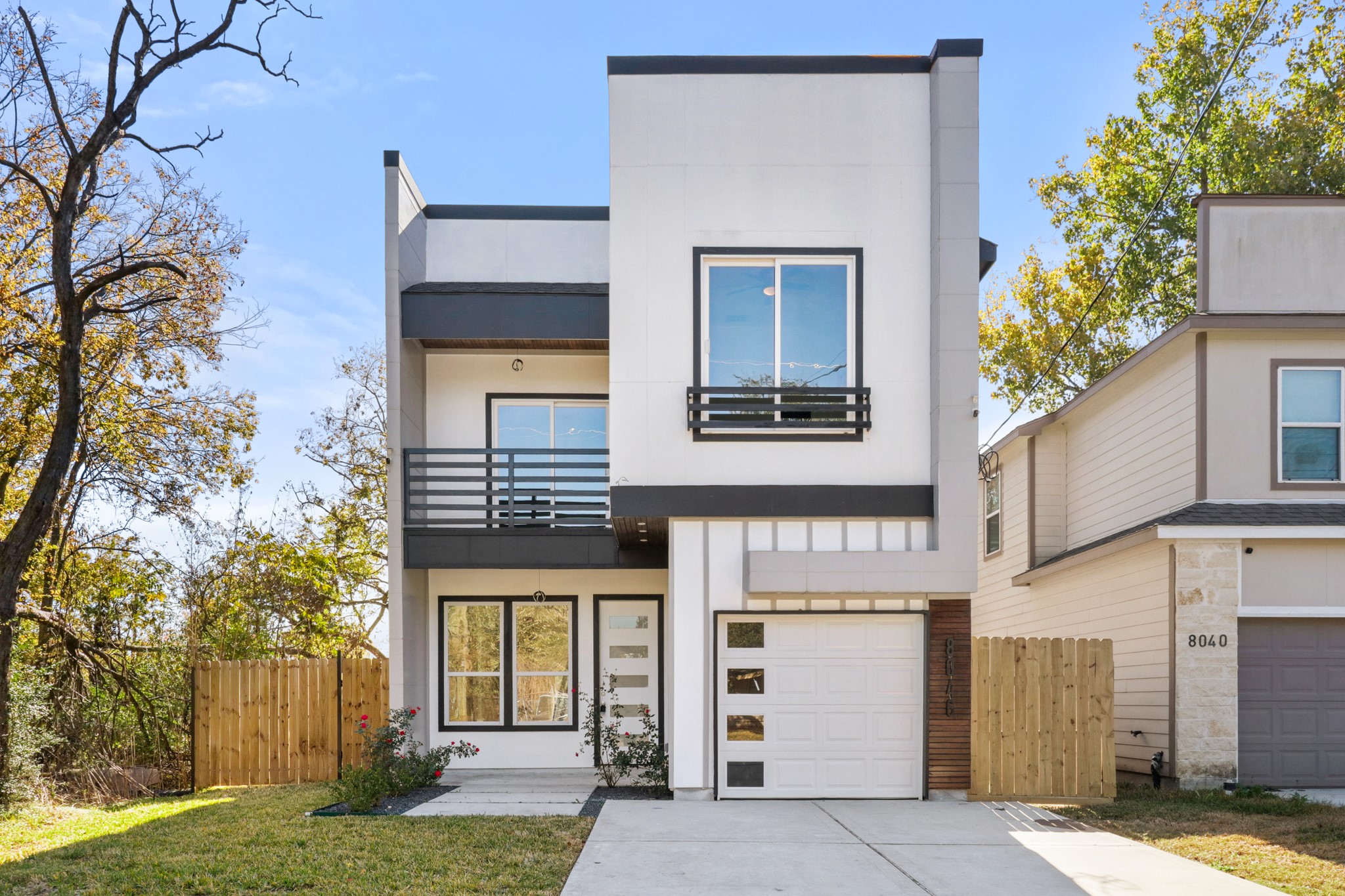 8046 Chateau Street Houston, TX 77028 - Photo 1 of 22 Modern two-story home with a sleek facade, featuring large windows and a balcony. It includes a one-car garage and is framed by a wooden fence and a small lawn, offering a clean, contemporary look.