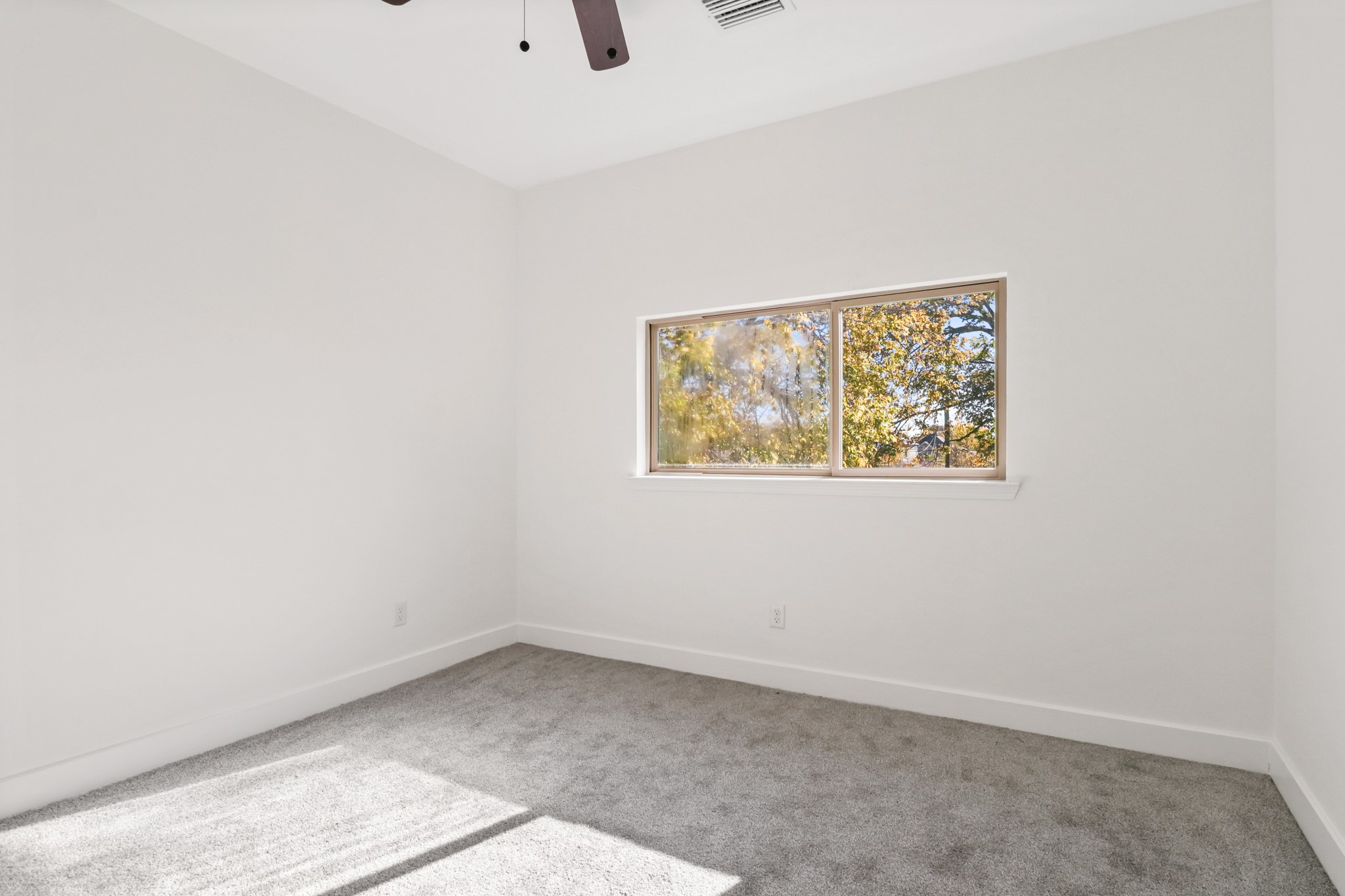 8046 Chateau Street Houston, TX 77028 - Photo 17 of 22 Bright, neutral bedroom with soft carpet and a large window offering a view of trees, creating a serene atmosphere. Ceiling fan included for comfort.