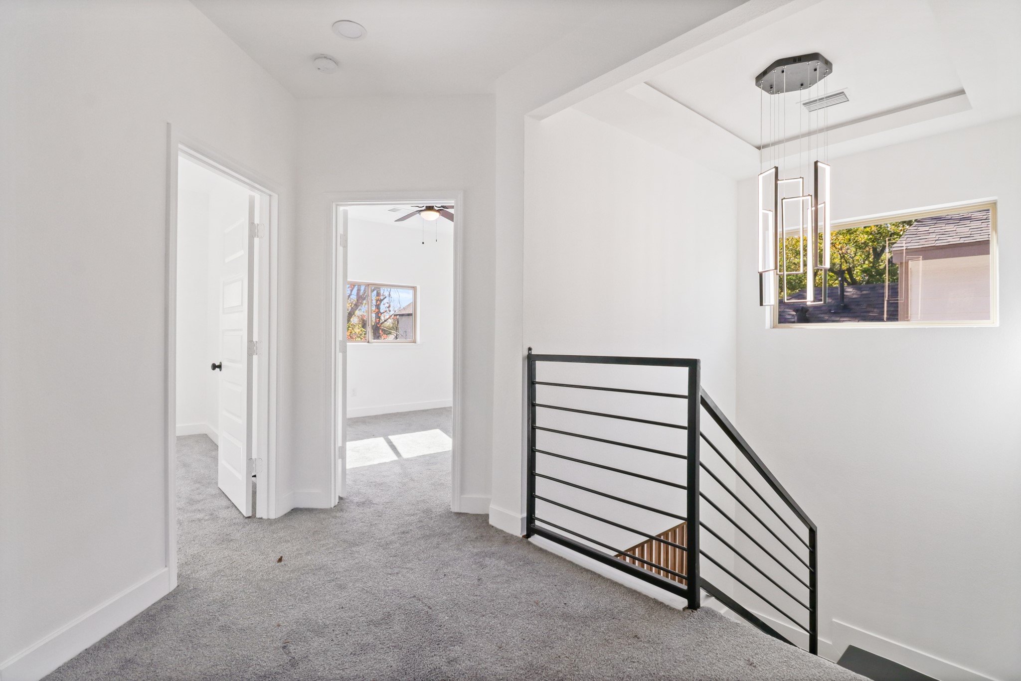8046 Chateau Street Houston, TX 77028 - Photo 20 of 22 Bright and modern hallway with carpeted floors, leading to two rooms. Features a sleek black railing along the staircase and a stylish geometric light fixture. Natural light streams in through a window, highlighting the clean, white walls.