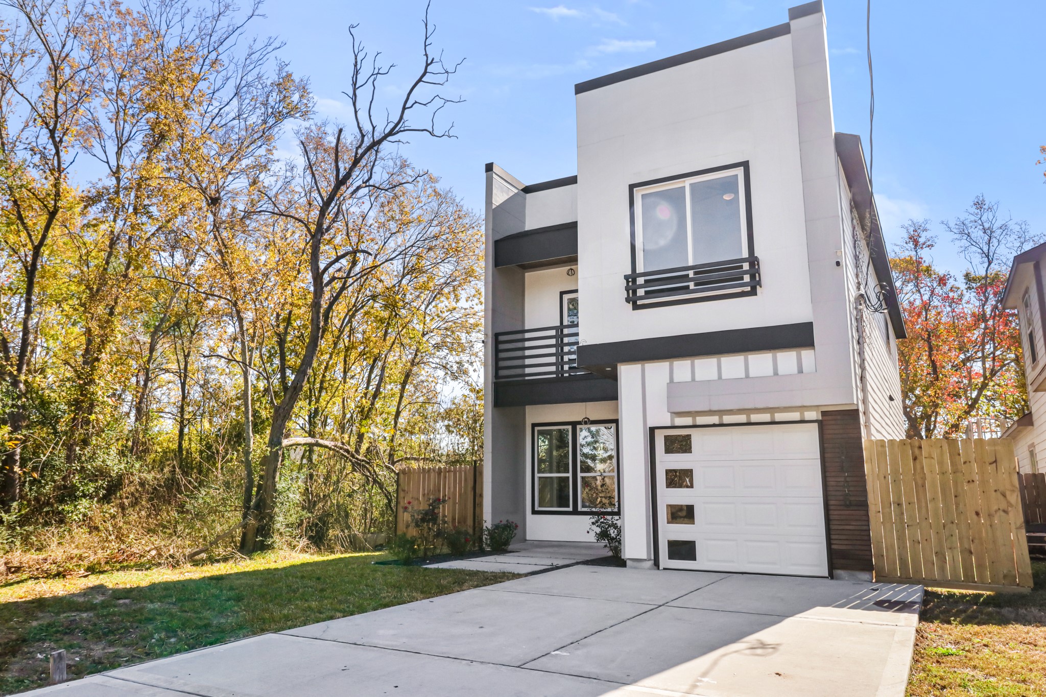 8046 Chateau Street Houston, TX 77028 - Photo 2 of 22 Modern two-story home with a sleek facade, featuring large windows and a single-car garage. It is set against a backdrop of mature trees, offering a blend of nature and contemporary living. The driveway provides ample parking space.