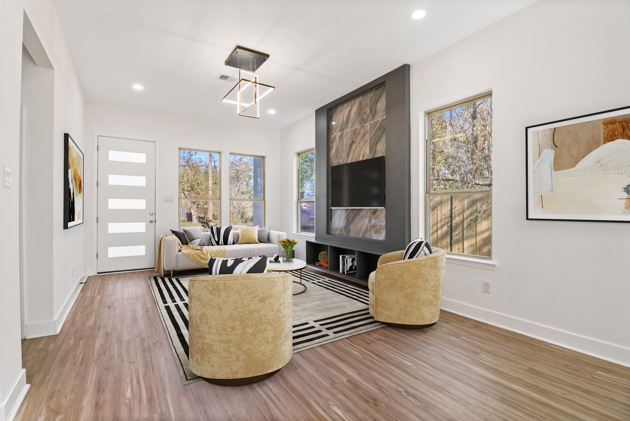 8046 Chateau Street Houston, TX 77028 - Photo 5 of 22 This inviting living room features modern design with a sleek ceiling light fixture, large windows for natural light, and a stylish accent wall with a mounted TV. Neutral tones and wood flooring create a warm, contemporary atmosphere.