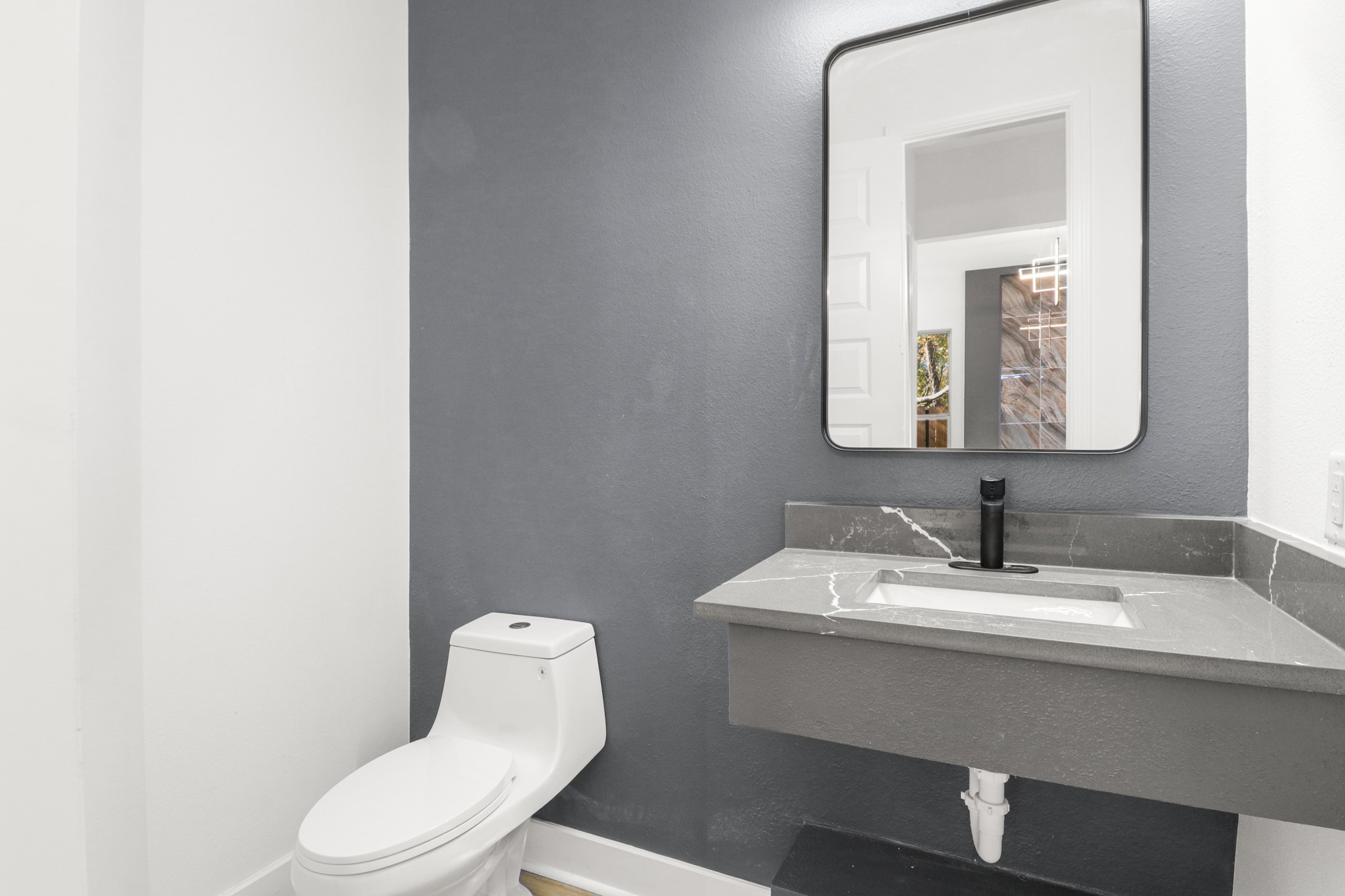 8046 Chateau Street Houston, TX 77028 - Photo 10 of 22 Modern half-bathroom with a sleek gray accent wall, wall-mounted mirror, and minimalist fixtures. Features a contemporary toilet and a gray countertop with integrated sink and black faucet.