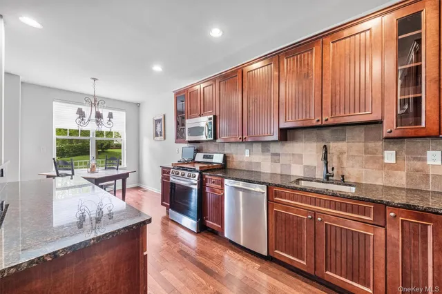 a kitchen with stainless steel appliances granite countertop wooden cabinets a sink dishwasher a stove and a refrigerator with wooden floor