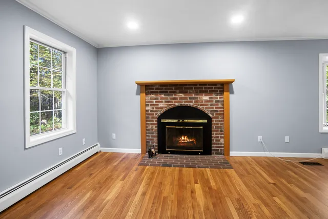a view of an empty room with wooden floor fireplace and a window