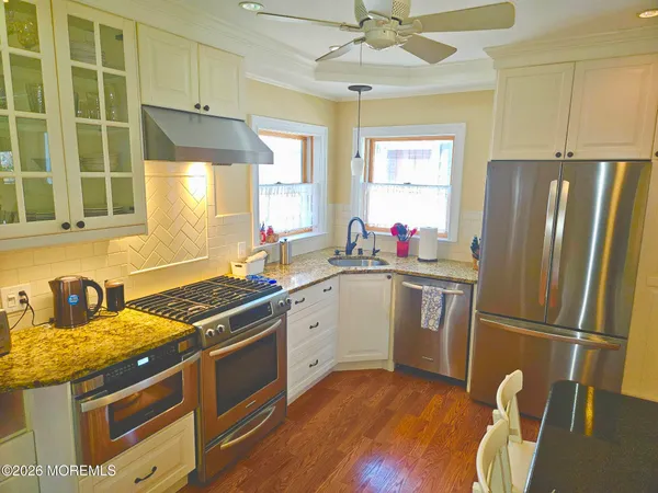 a kitchen with stainless steel appliances granite countertop a refrigerator a sink dishwasher a stove with white cabinets and wooden floor