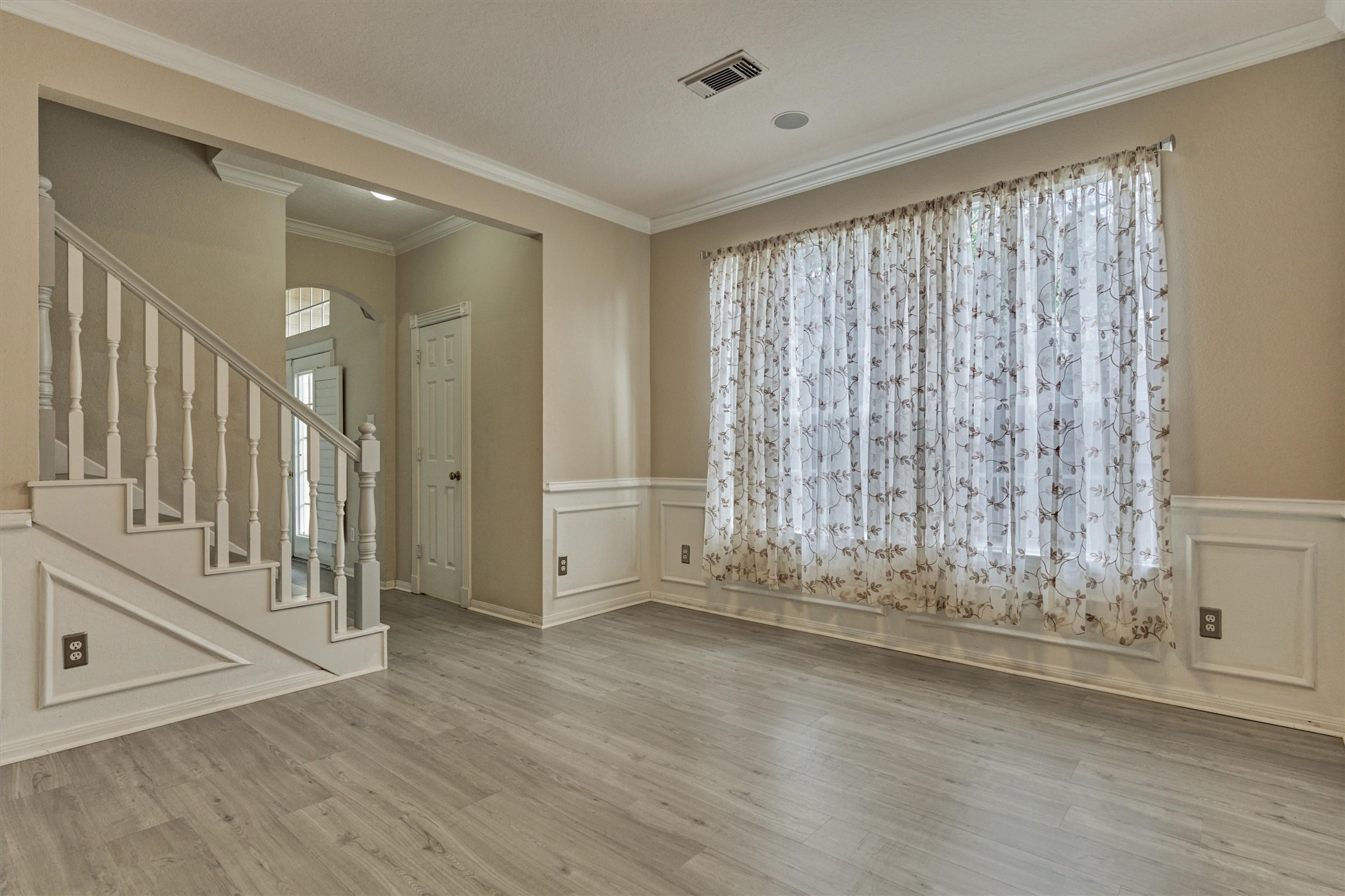 14420 Walters Road, Unit 26 Houston, TX 77014 - Photo 19 of 45 A bright, inviting room featuring light wood-look flooring and elegant wainscoting. Large, floral-patterned curtains allow natural light to filter through. The space is complemented by a classic staircase with white railing, creating a warm and welcoming atmosphere.