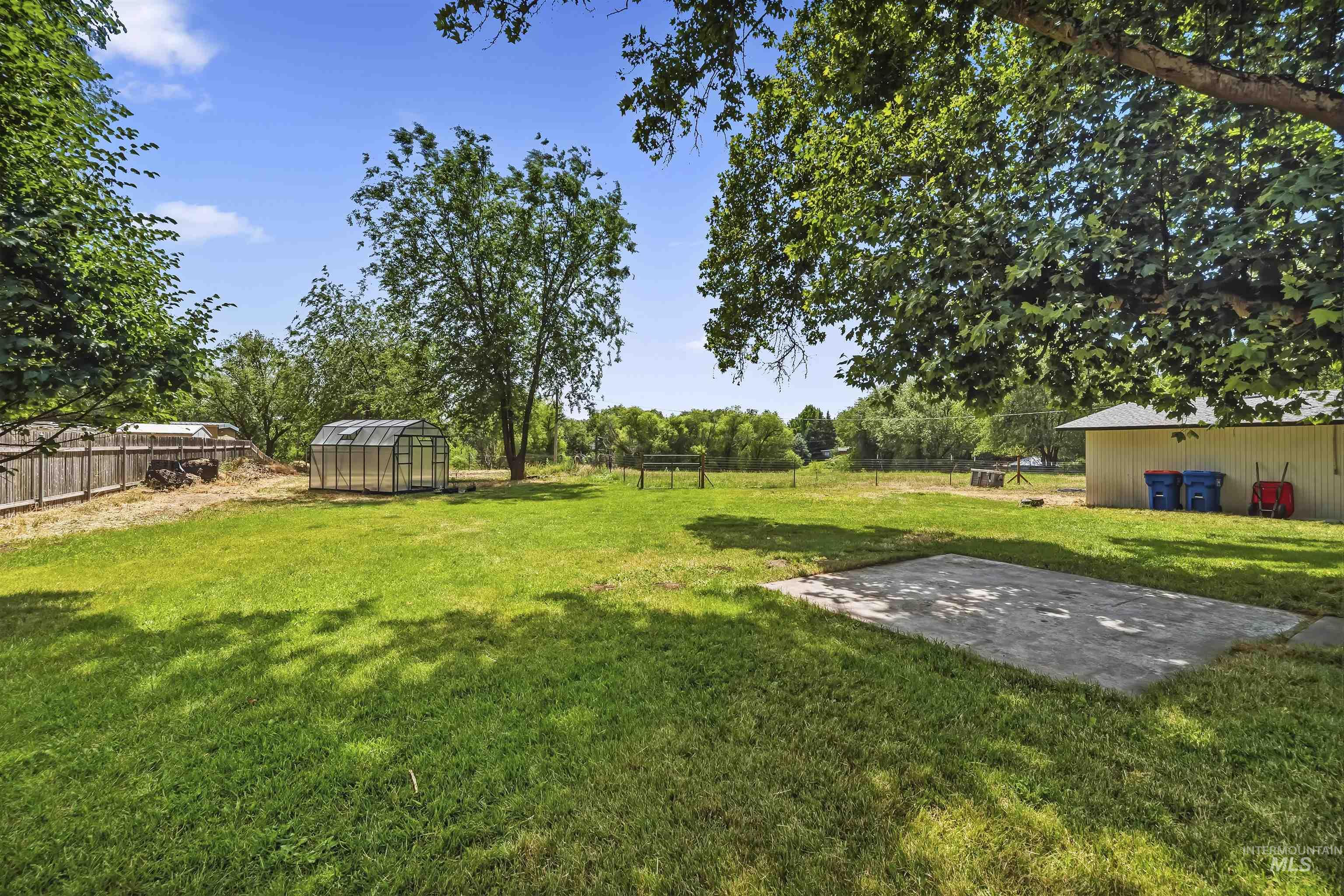 355 East Beacon Light Road Eagle, ID 83616 - Photo 28 of 47 Expansive grassy yard featuring a greenhouse, mature trees, a concrete pad, a wood fence, and a distant outbuilding