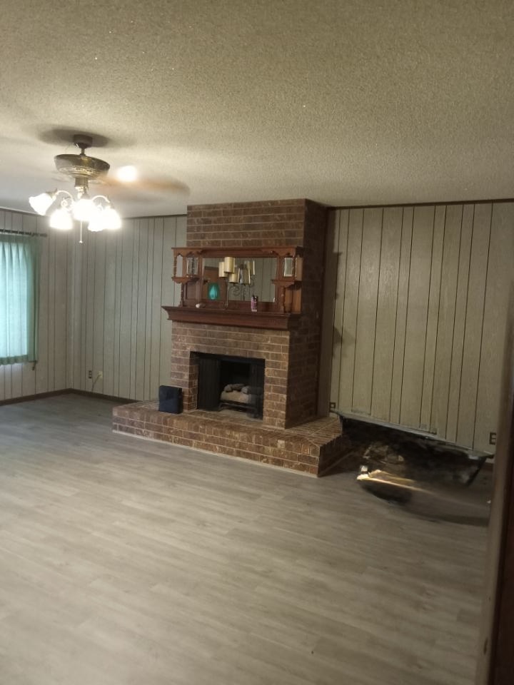 709 West 11th Street Elgin, TX 78621 - Photo 9 of 12 Unfurnished living room featuring wood walls, a ceiling fan, a textured ceiling, a fireplace, and wood finished floors