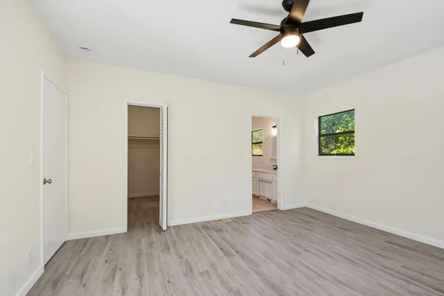 an empty room with wooden floor ceiling fan and windows