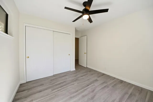 an empty room with wooden floor closet and fan