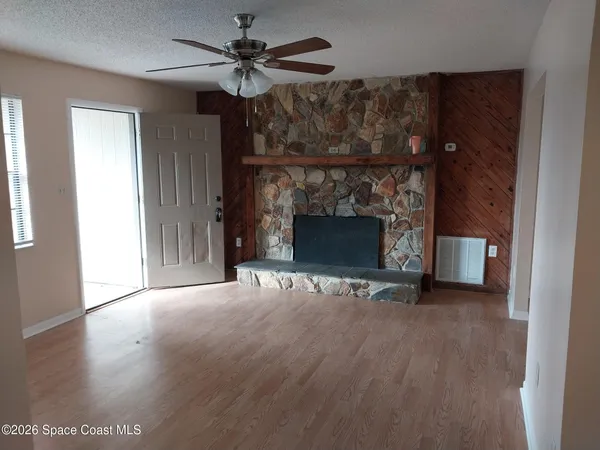 a view of an empty room with wooden floor fireplace and a window