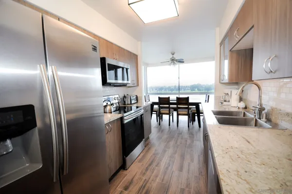 a kitchen with granite countertop stainless steel appliances a dining table chairs sink and wooden floor