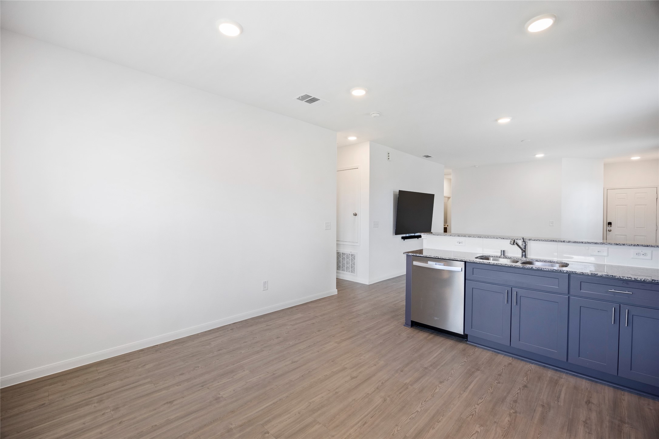 17907 Grain Auger Road Hockley, TX 77447 - Photo 13 of 24 bright, open-concept living space with light wood flooring and recessed lighting. The modern kitchen features a dark blue island with a double sink and stainless steel dishwasher, seamlessly integrating with the living area.