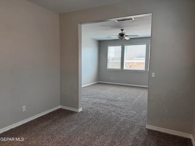 an empty room that has a chandelier fan and a window