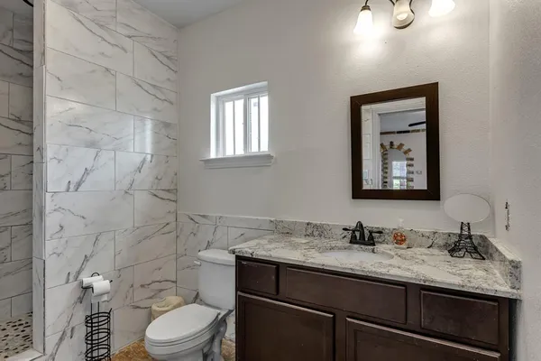 a bathroom with a granite countertop sink toilet and painting on the wall