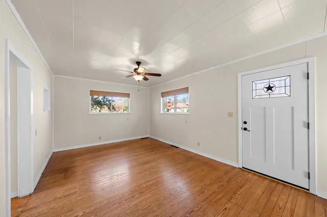 an empty room with wooden floor chandelier fan and windows