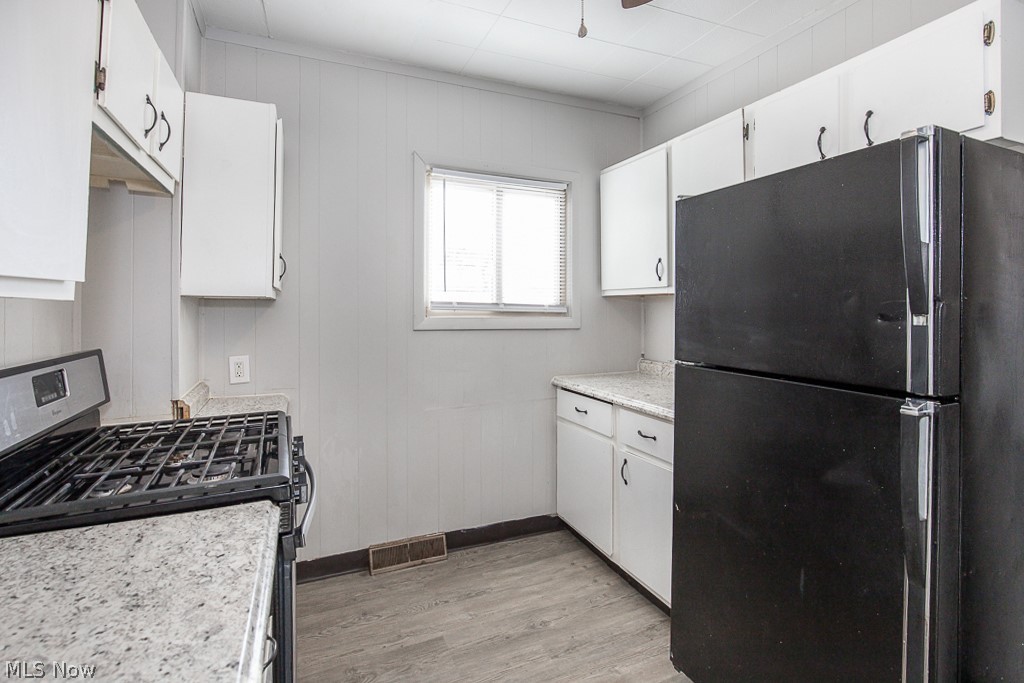 4661 Horton Road Cleveland, OH 44125 - Photo 9 of 27 Kitchen with light hardwood / wood-style floors, white cabinets, gas range oven, and black refrigerator