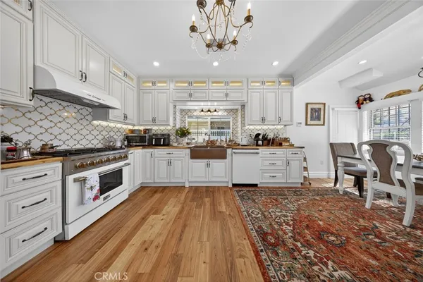 a kitchen with granite countertop a stove top oven a sink dishwasher and white cabinets with wooden floor