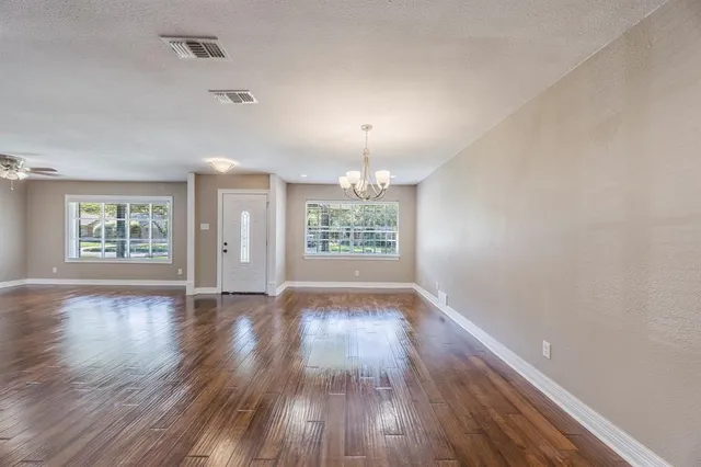 an empty room with wooden floor chandelier and windows