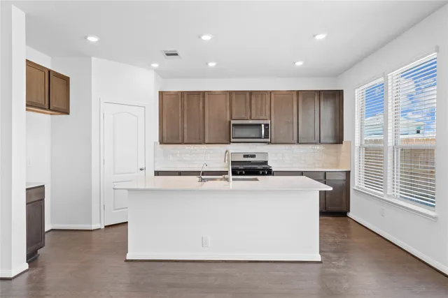 a kitchen with kitchen island a stove a sink a refrigerator white cabinets and wooden floor