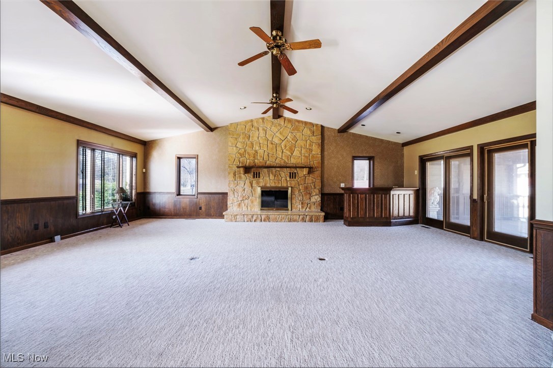 7059 Stewart Sharon Road Hubbard, OH 44425 - Photo 7 of 49 Unfurnished living room with a wainscoted wall, wood walls, a stone fireplace, and lofted ceiling with beams