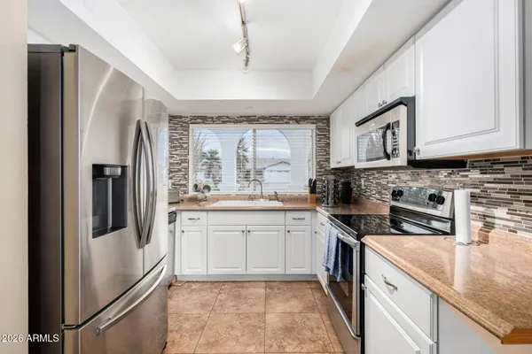 a kitchen with stainless steel appliances granite countertop a refrigerator a sink a stove and white cabinets with wooden floor