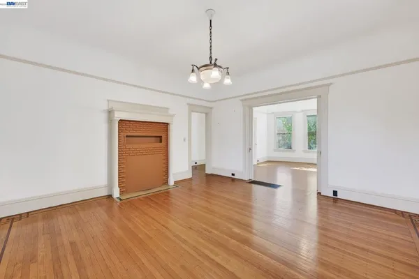 an empty room with wooden floor chandelier and windows