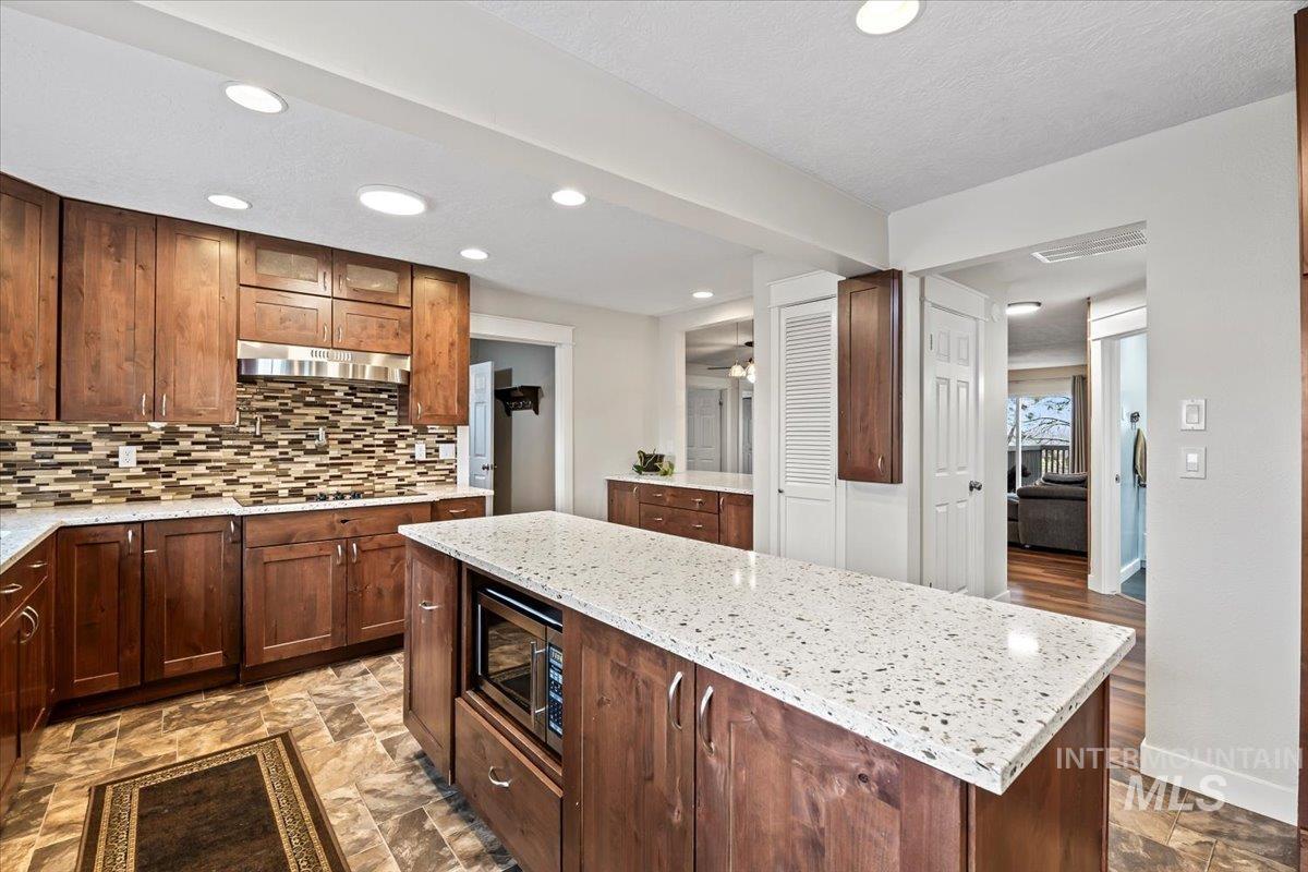 11545 Kuna Road Kuna, ID 83634 - Photo 16 of 50 Kitchen featuring light stone counters, stone finish flooring, a center island with microwave, recessed lighting, and stainless steel dishwasher, double oven and separate stove top and pot filler