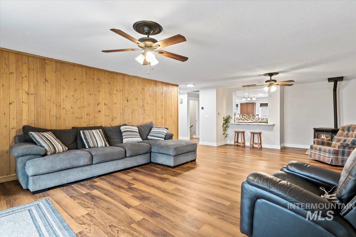 11545 Kuna Road Kuna, ID 83634 - Photo 21 of 50 Living room featuring a wood stove, wood finished floors, ceiling fan, and wood walls and wood stove