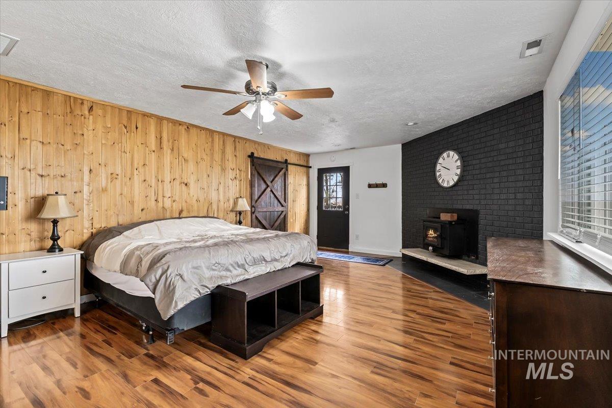 11545 Kuna Road Kuna, ID 83634 - Photo 8 of 50 Bedroom featuring wood fireplace, a barn door to primary bath/closet, wood finished floors, wooden accent walls, and door to outdoor deck