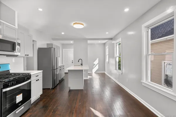 a kitchen with stainless steel appliances a refrigerator a stove top oven a sink dishwasher and white cabinets with wooden floor