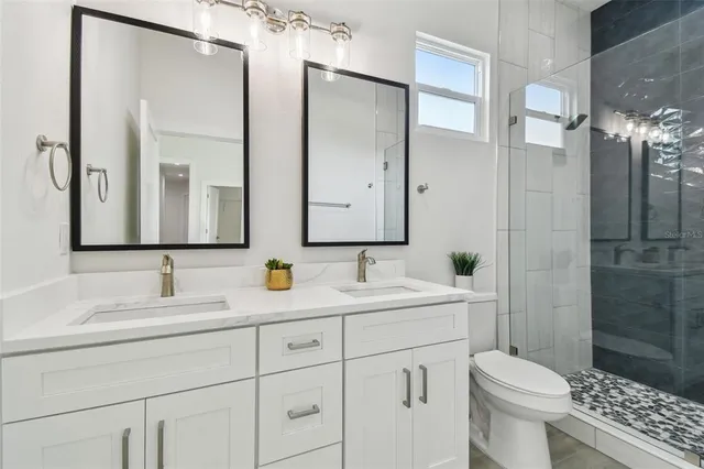 a bathroom with a double vanity sink toilet mirror and shower