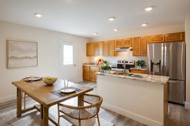 a kitchen with stainless steel appliances granite countertop a refrigerator a stove a sink a dining table and chairs with wooden floor