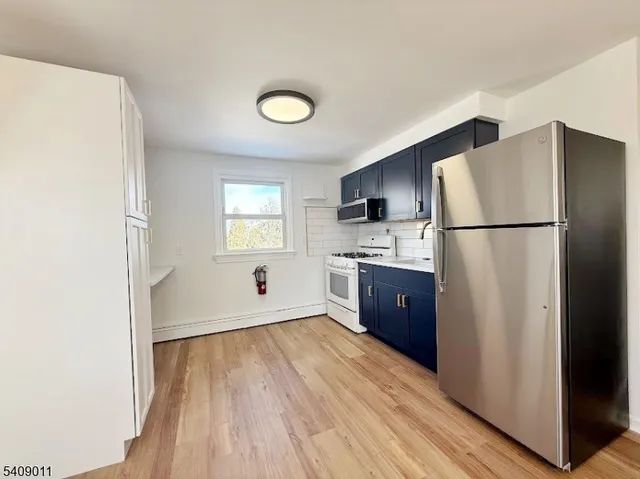 a kitchen with a refrigerator a stove top oven a wooden floor and a window