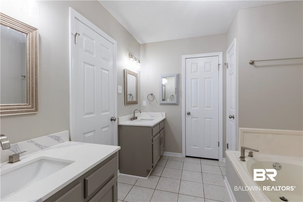 101 Lawson Road Daphne, AL 36526 - Photo 8 of 20 Bathroom featuring dual vanities with white countertops, a built-in tub with brushed nickel fixtures, light gray wall paint, and white tile flooring