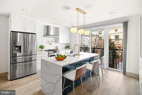 a kitchen with stainless steel appliances a dining table chairs a refrigerator and cabinets