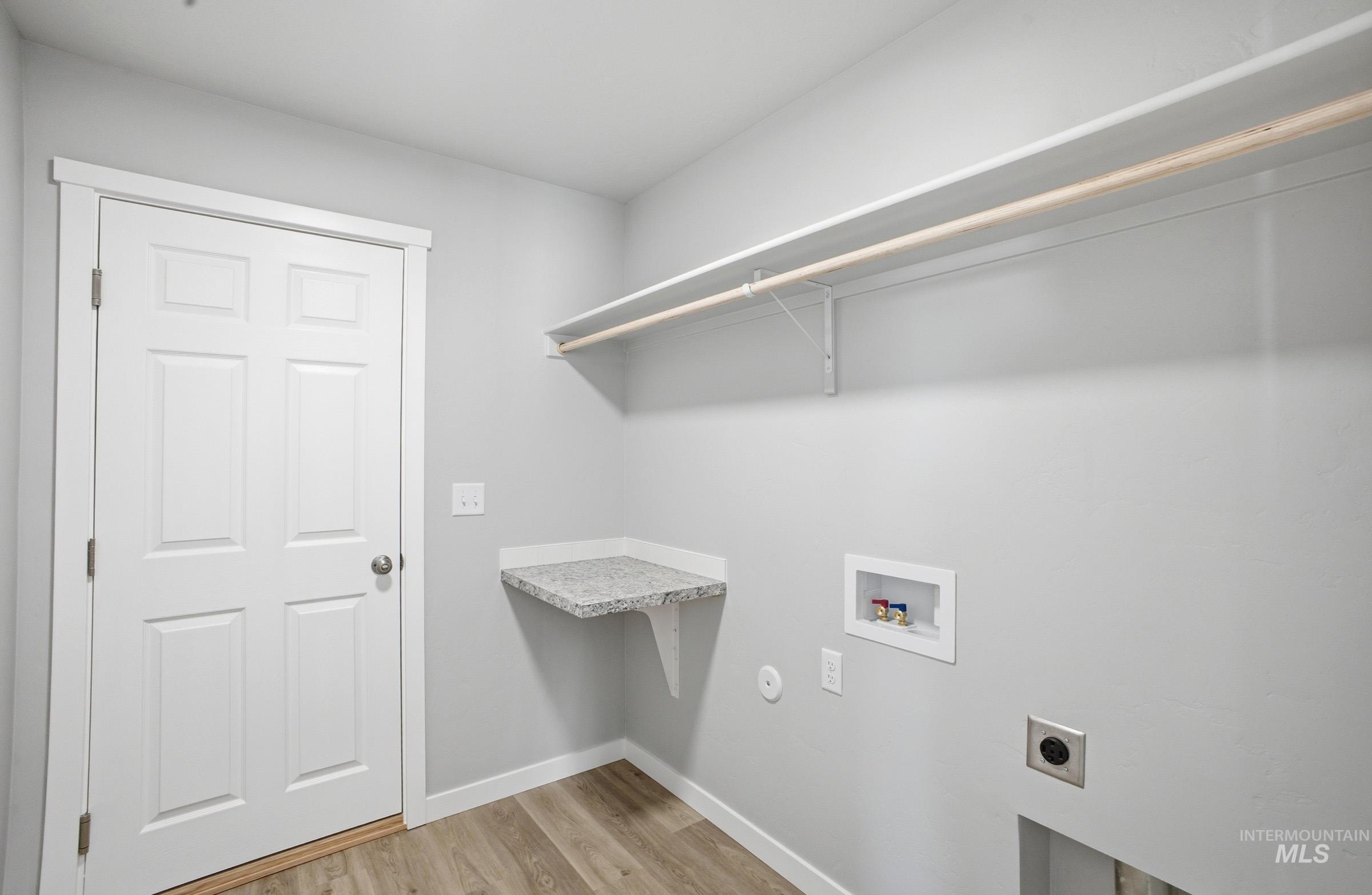 14106 Winding Street Caldwell, ID 83607 - Photo 14 of 18 Dedicated laundry area featuring wood-finish flooring, a six-panel door, built-in shelving, a built-in hanging rod, and a corner countertop with a stone-look finish